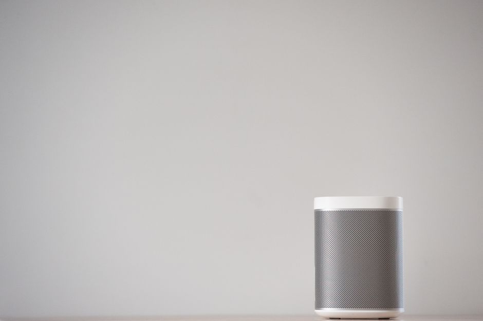A sleek, wireless smart speaker on a wooden table against a plain wall.